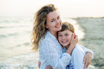 Young mother with little daughter near the sea. Beach with sand. Blue water.