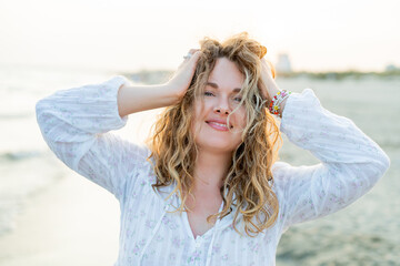 Young curly woman near the sea. Beach with sand. Blue water.