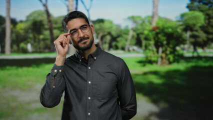 Hispanic man with glasses in a park setting, wearing a dark shirt, showcasing confidence and style...