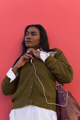 Young female student listening to music on pink background