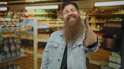 Young bearded man extends hand for handshake in supermarket aisle stocked with groceries;...