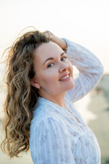 Young curly woman near the sea. Beach with sand. Blue water.