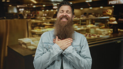 Fototapeta premium Young man with beard smiling broadly places hand on chest in busy indoor restaurant; gratitude sincerity.