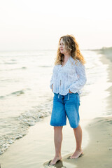 Young curly woman near the sea. Beach with sand. Blue water.