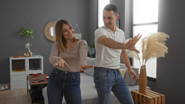 Couple dancing happily in their stylish living room, capturing a joyful moment indoors with a modern home interior, reflecting love and togetherness. - Powered by Adobe
