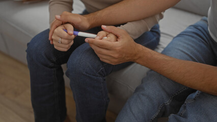 Couple sitting together on a couch in their home holding a pregnancy test, symbolizing love,...