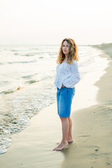Young curly woman near the sea. Beach with sand. Blue water.