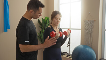 Man and woman exercising with dumbbells in a gym, focusing on fitness and strength training indoors...