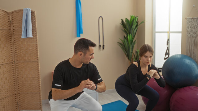 Man and woman exercising indoors at a gym with fitness balls and equipment emphasizing athletic training and teamwork in a motivating environment.