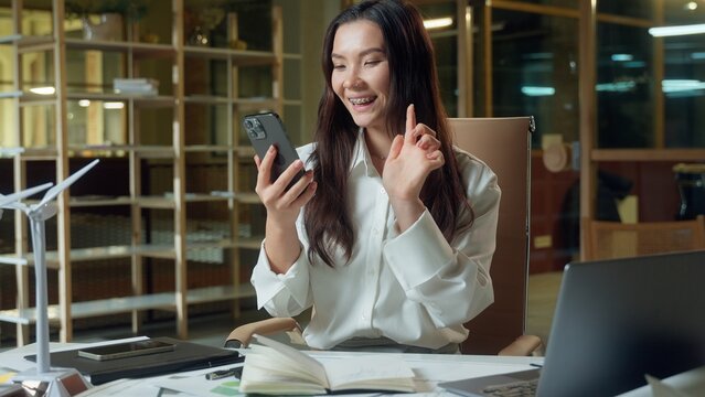 Happy smiling Asian woman Chinese businesswoman architect business employer texting mobile phone message scrolling social media addict Korean Japanese female girl user smartphone online work in office