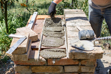 A hand applies mortar with a trowel to prepared brick surfaces for the next layer