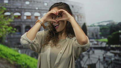 Woman forming heart with hands outside roman coliseum smiling happily near ancient iconic landmark...