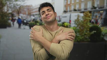 Man lifts arms hugging his chest on a busy street showing young hispanic smiling confidence as a...