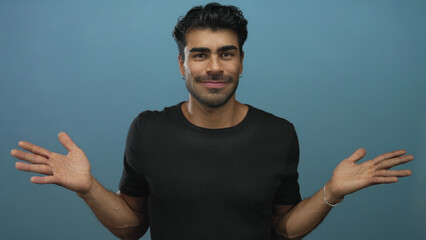 Man shows open palms and extends both hands toward camera against a smooth blue studio wall;...