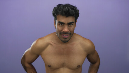 Young hispanic man leaning forward with bare chest and hands on hips in purple studio; physical...