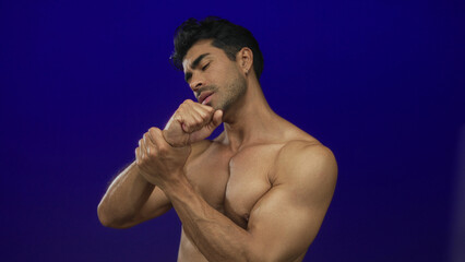Man holds wrist with tense grip and pained expression in studio setting with deep blue backdrop;...