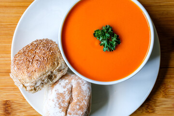 A Bowl Of Healthy Tomato Soup With Parsley Garnish And Bread Rolls