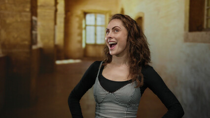 Young woman smiling in an old university hallway with sunlight streaming through large windows, creating a warm and welcoming atmosphere indoors.