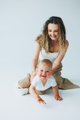 Young mother on a white background playing with her one-year-old son. Toddler boy and mother laughing hugging. Happy mother with child.