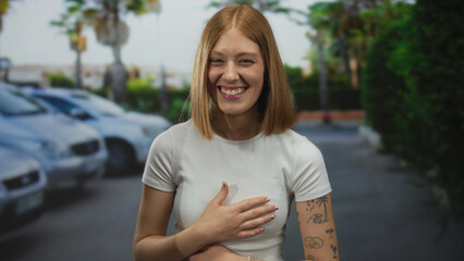 Young woman smiling outdoors surrounded by parked cars on a sunny city street, exuding happiness...