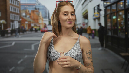 Young blonde woman in sunglasses and swimsuit poses confidently on a bustling urban street, exuding...