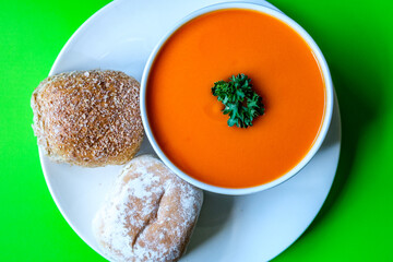 A Bowl Of Healthy Tomato Soup With Parsley Garnish And Bread Rolls