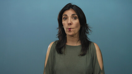 Middle aged hispanic woman in olive green top with dark hair purses lips and tilts head in studio;...