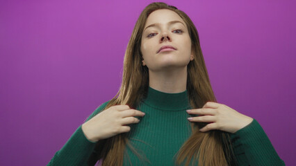 Woman touching hair against purple studio wall while wearing a green sweater and long red hair...