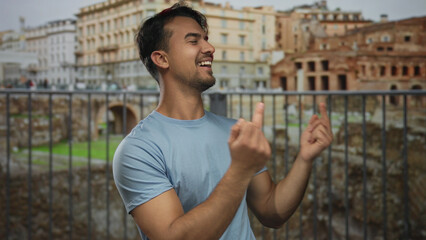 Hispanic man making gestures with middle fingers while laughing in front of roman ruins in an...