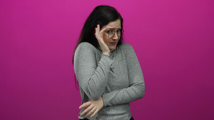 Woman with brunette hair and glasses in a gray top expresses fear or surprise against a vibrant...