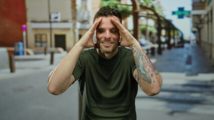 Man gesturing playfully with tattoos in an urban street background, wearing a green shirt, exuding...