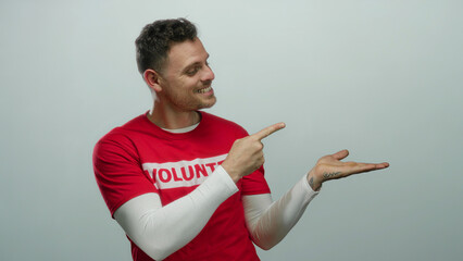 Young man with tattooed hand and volunteer shirt gestures on isolated white background pointing...