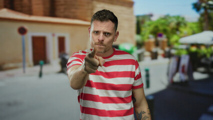 Young man in red striped shirt gestures expressively on urban street with tattoos visible on arm
