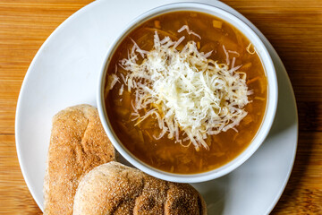 A Bowl Of Traditional French Onion Soup Topped With Grated Cheese And Wholemeal Submarine Bread Rolls