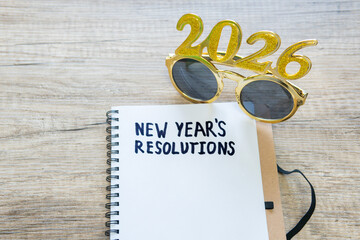 New year resolutions 2026 on desk. Shiny glasses 2026 and list of resolutions with paper and pen...