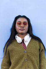 Woman with headphones and sunglasses posing against a blue background.