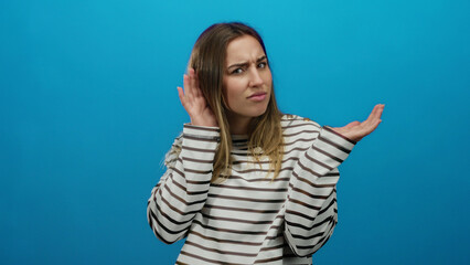 Woman wearing striped shirt against blue background shows confused expression, conveying...