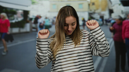 Fototapeta premium Smiling young blonde woman stands on a lively city street wearing a striped shirt, capturing the essence of a cheerful outdoor urban environment.