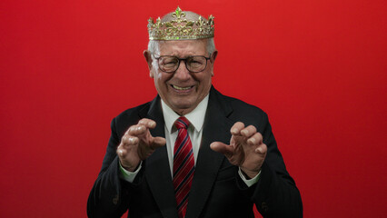 Senior man in business suit and crown making scared expressions against a vibrant red background,...