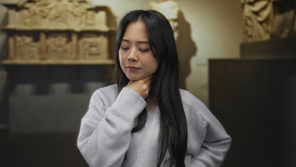 Young woman indoors at museum experiencing discomfort with hand on neck amid historical artifacts...