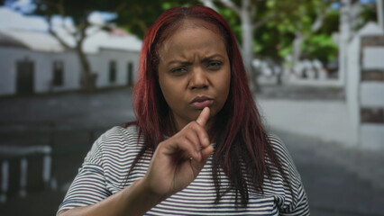 Young african american woman points her extended finger in a refusal gesture on a city street;...