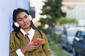 Young african listening to music leaning against a blue wall