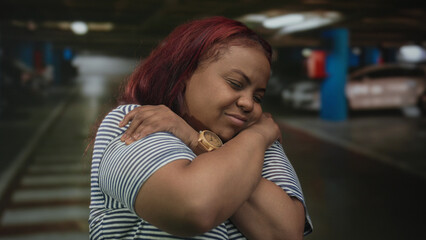 Woman wearing wooden watch hugs shoulders with crossed arms inside a parking building; self care...