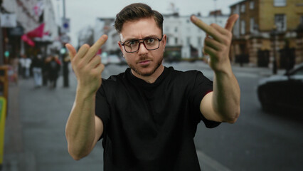 Young bearded man on a city street making a rude hand gesture with both middle fingers raised while...
