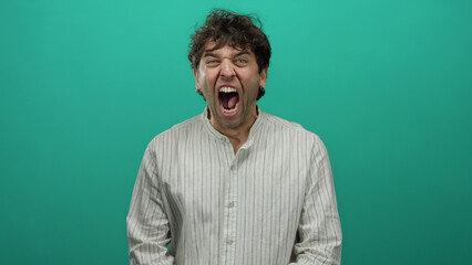 Handsome hispanic man shouting with expression against a vibrant green background, wearing a...