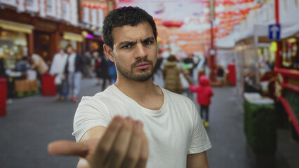 Obraz premium Man with serious expression beckons with outstretched hand and points finger on colorful street; invitation connection.