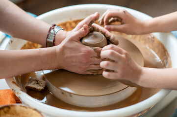 Hands of child and adult shaping clay together on pottery wheel