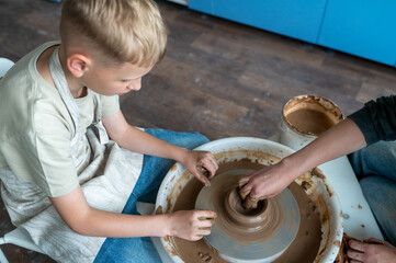 Boy sculpting clay on pottery wheel, children's activity with teacher