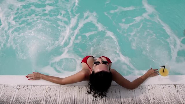 Young beautiful woman in a red swimsuit relaxing in a jacuzzi with a cocktail. Concept spa, relaxation and leisure.