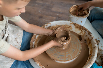 Boy and female instructor shaping clay together at pottery wheel, kids learning traditional craft